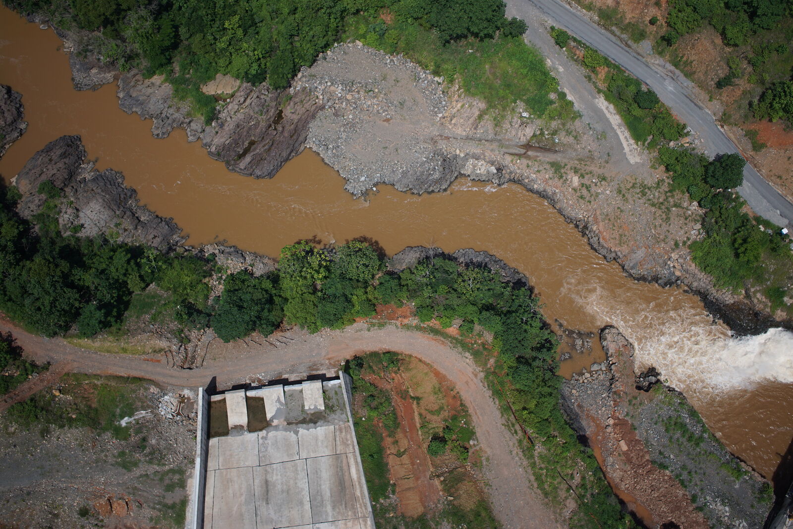 Vista aérea de un río de aguas turbias junto a una obra hidráulica y su entorno vegetado